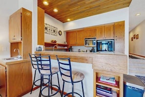 A kitchen with wooden cabinets, a microwave, a sink, and two bar stools. - Charming 2BR Lakefront - Patio - Pool (Chelan)