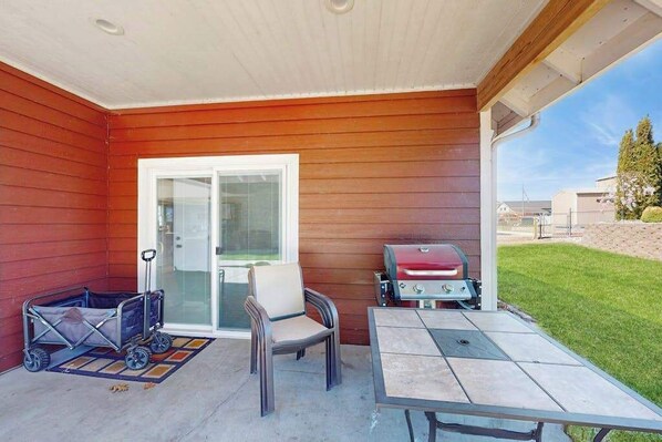 A covered patio with a grill, a stroller, and a table.