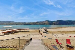A beach with a wooden walkway leading to the water, picnic tables, and red chairs.