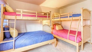 Ein Schlafraum mit Etagenbetten, zwei Ebenen, jeweils mit einer Leiter, und einem Einzelbett unten.