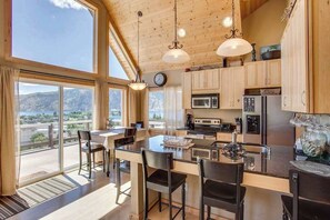 Une cuisine moderne avec des meubles en bois, un îlot central et une vue sur les montagnes grâce à de grandes fenêtres.