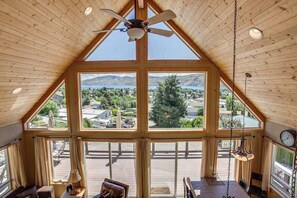 A room with a sloped ceiling, large windows, a ceiling fan, and a dining area. - Lovely 3BR Lakeview - Deck - Ping Pong - W&D (Manson)