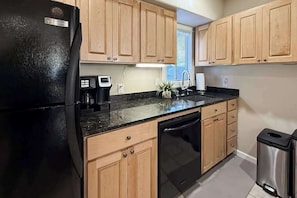 A kitchen with wooden cabinets, a black refrigerator, a dishwasher, and a trash bin.