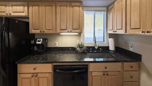 A kitchen with wooden cabinets, a black refrigerator, a dishwasher, a sink, and a window with blinds. - 1BR condo with pool, hot tub & great location (Chelan)