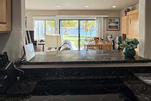 A kitchen with a marble countertop, a dining area with chairs and a table, and a view through glass doors to an outdoor space.