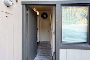 A narrow hallway with a door at the end, a light fixture above, and a wreath on the wall.