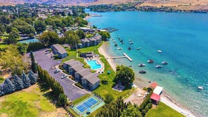 An aerial view of a lakeside property with a swimming pool, tennis court, and dock with boats. - 1BR condo with pool, hot tub & great location (Chelan)