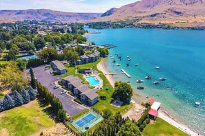 Eine Luftaufnahme eines Sees mit einem Anwesen, das einen Swimmingpool, einen Tennisplatz und einen Steg mit Booten umfasst.