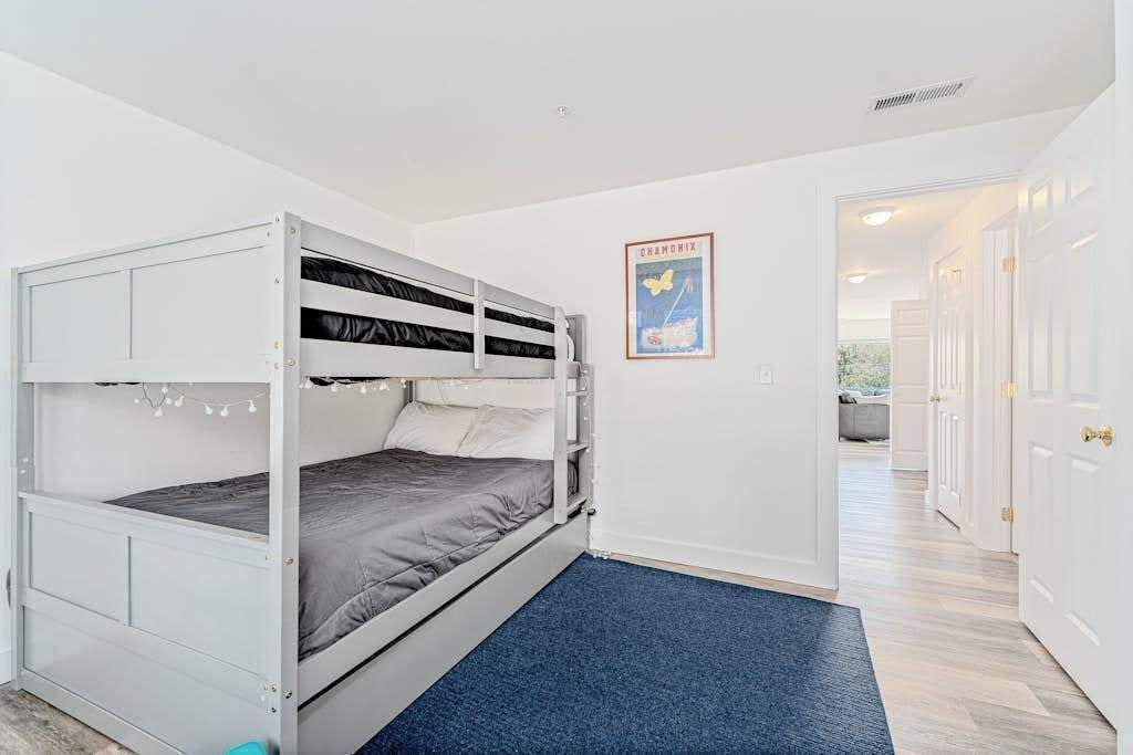 Quarto com beliches, carpete azul, paredes brancas e um quadro na parede.