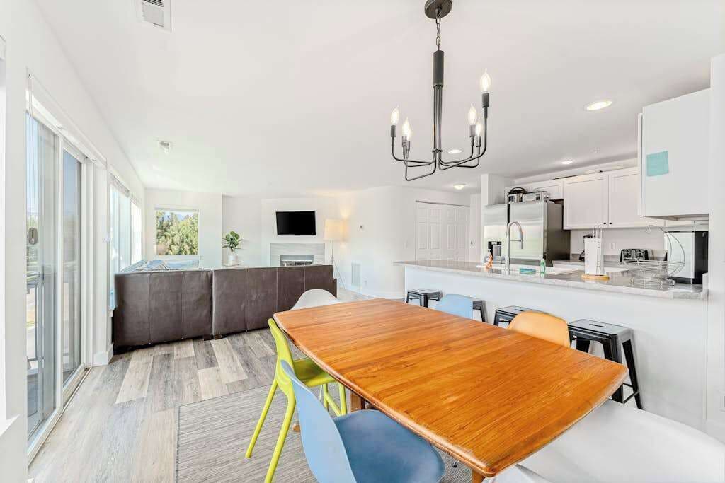 A modern kitchen with white cabinets, a central island, and a dining area with a wooden table and chairs.