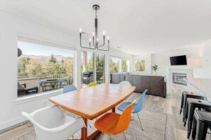 A modern kitchen with a dining area, large windows, and a view of the outdoors.