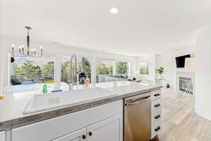 A modern kitchen with a large island, white cabinetry, and a view of the outdoors.
