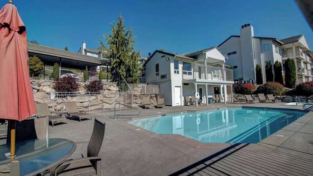 A swimming pool with lounge chairs and a covered area, surrounded by buildings and a tree. - Downtown 2BR - Patio - Pool - Washer/Dryer (Chelan)