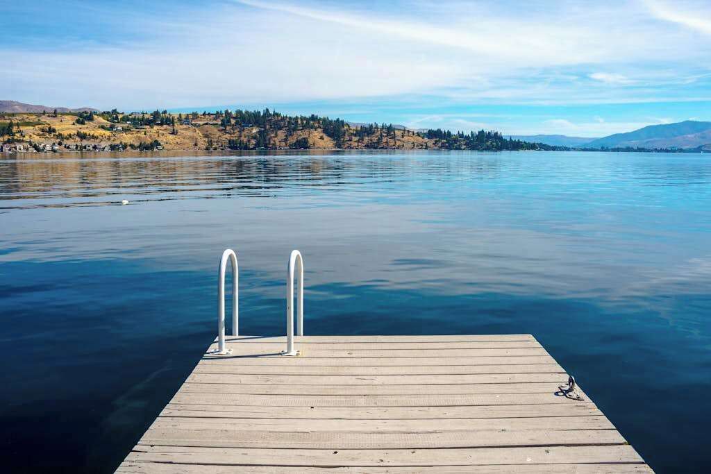 A wooden dock extending into calm water with a clear view of a hilly landscape in the distance.