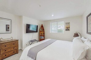 A bedroom with a bed, a television mounted on the wall, a wooden bookshelf, a window with blinds, and a welcome sign. - Downtown 2BR - Patio - Pool - Washer/Dryer (Chelan)