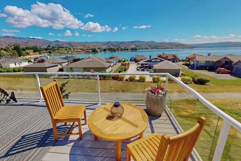 A balcony with a round table and chairs, overlooking a residential area and a body of water.