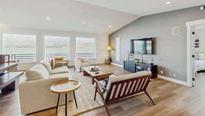 A spacious living room with a large window, a sofa, a coffee table, and a television. - Gorgeous 3BR Lakefront - Dock - WoodStove (Chelan)