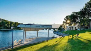 A pavilion named 'Riverwalk Pavilion' by a body of water with a grassy area and a bridge in the background. - Comfy 1BR Lakefront - Patio - Pool - (Chelan)