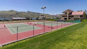 A tennis court with a net, surrounded by a fence, and a building with a flat roof in the background. - Comfy 1BR Lakefront - Patio - Pool - (Chelan)