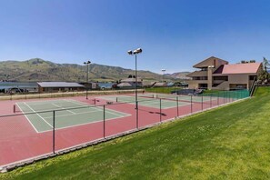A tennis court with a net, surrounded by a fence, and a building with a flat roof in the background. - Comfy 1BR Lakefront - Patio - Pool - (Chelan)