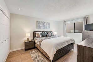 A bedroom with a bed, bedside tables, a TV, and a window with curtains. - Comfy 1BR Lakefront - Patio - Pool - (Chelan)