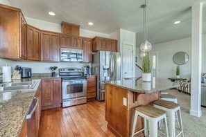 A modern kitchen with wooden cabinets, stainless steel appliances, and a granite countertop. - 3BR Riverview Townhome with shared hot tub & pools (Quincy)