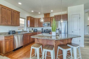 A modern kitchen with wooden cabinets, stainless steel appliances, and a central island with bar stools. - 3BR Riverview Townhome with shared hot tub & pools (Quincy)