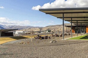 A modern building with a covered outdoor seating area, a gravel courtyard, and a mountainous backdrop. - 3BR Riverview Townhome with shared hot tub & pools (Quincy)