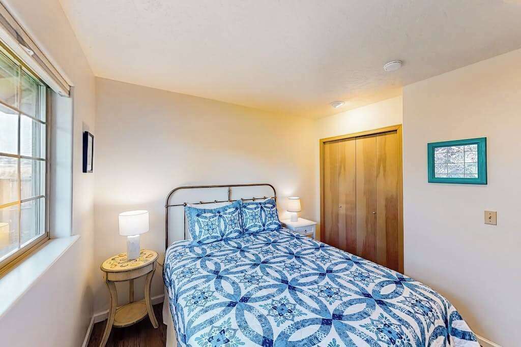 Um quarto com cama, mesas de cabeceira, uma janela e uma porta.