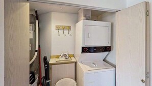 Uma área de lavanderia compacta com máquina de lavar e secadora, um balcão pequeno e um varal fixado na parede.