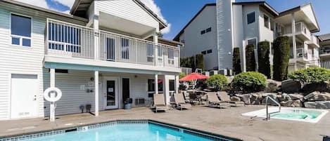 A swimming pool area with lounge chairs and umbrellas, surrounded by buildings with balconies.