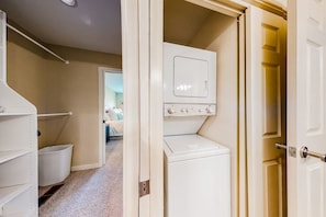 A laundry room with a washer and dryer, a white shelf unit, and a hallway leading to another room. - 1BR Lakefront 2nd-Floor - Balcony - Pool (Chelan)