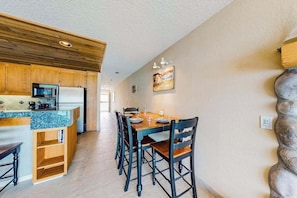 A kitchen with wooden cabinets, a granite countertop, and a dining area with a wooden table and chairs. - 1BR Lakefront 2nd-Floor - Balcony - Pool (Chelan)