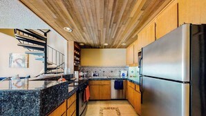 Eine Küche mit Holzbalkendecke, Granit Arbeitsplatten, einem Edelstahl-Kühlschrank und einem Einbauofen.