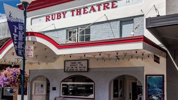 Ein Theater mit einer Litfaßsäule, auf der 'RUBY THEATRE' steht, und einem Schild mit der Aufschrift 'Kein Parken von 3 bis 6 Uhr morgens'.