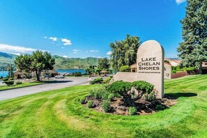 Ett bostadsområde med en skylt som visar vägen till Lake Chelan Shores, en välskött gräsmatta och utsikt över det omgivande landskapet.