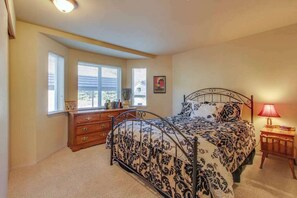 A bedroom with a bed, dresser, windows, and a lamp.