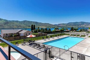 Piscina com espreguiçadeiras e vista para um lago e colinas.