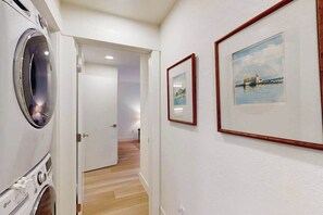 Uma área de lavanderia com máquina de lavar, um corredor que leva a outro quarto e duas quadros na parede.