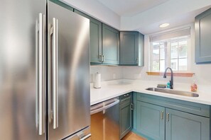 Una cocina con refrigerador de acero inoxidable, gabinetes color turquesa, encimera blanca y una ventana con vistas.