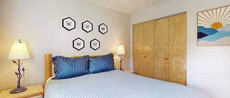 Quarto com cama, duas mesas de cabeceira com luminárias, guarda-roupa e quadros na parede.