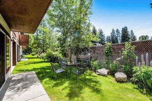 A patio with a table and chairs, surrounded by a well-maintained lawn and a wooden fence. - 2BR 1st-Floor - Icicle Village Resort Condo (Leavenworth)