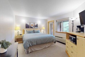 Habitación de hotel con cama, lámparas de noche, televisor, calefacción y ventana con vistas.