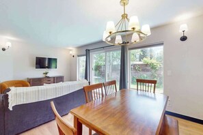 Un coin repas avec une table et des chaises en bois, un lustre et un téléviseur posé sur un meuble.