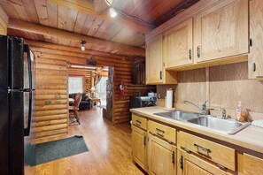 A log cabin interior with a kitchen area featuring wooden cabinets, a sink, and a refrigerator. - 1BR Lakeview - WoodStove - Deck - Firepit - W&D (Leavenworth)