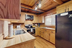 Una cocina con armarios de madera, un lavamanos de acero inoxidable, un microondas, una estufa y un refrigerador.