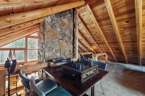 A wooden interior with a stone wall, a chessboard, and a table with chairs. - 1BR Lakeview - WoodStove - Deck - Firepit - W&D (Leavenworth)