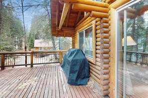 A wooden deck with a covered grill, a glass door, and a view of a forested area. - 1BR Lakeview - WoodStove - Deck - Firepit - W&D (Leavenworth)