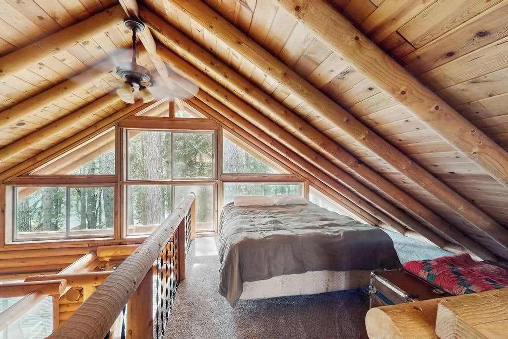 A wooden cabin with a loft bedroom featuring a bed, a window, and a ceiling fan.