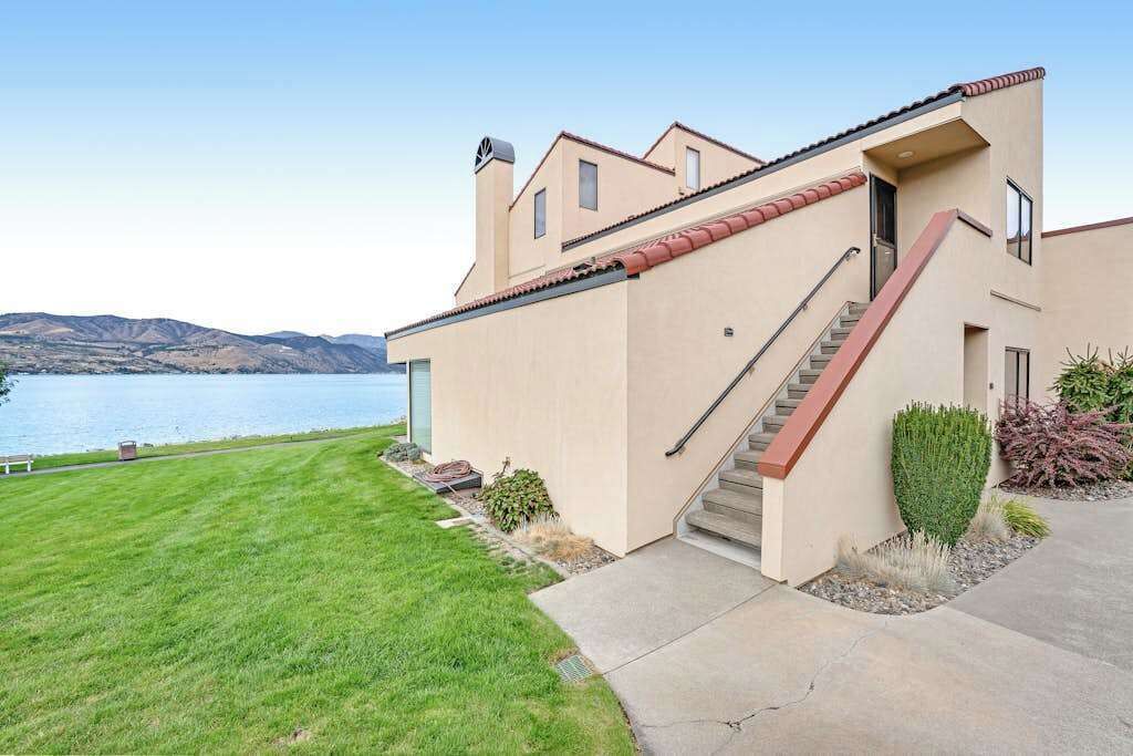 Een modern huis met een trap naar een deur, een verzorgd gazon en uitzicht op het water.